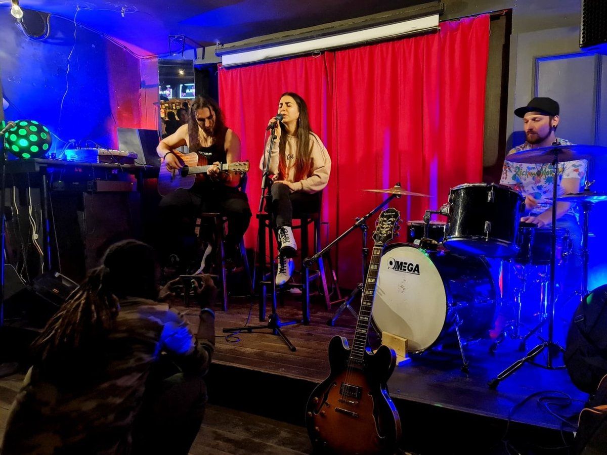 Naira singing on stage with a guitarist and a drummer